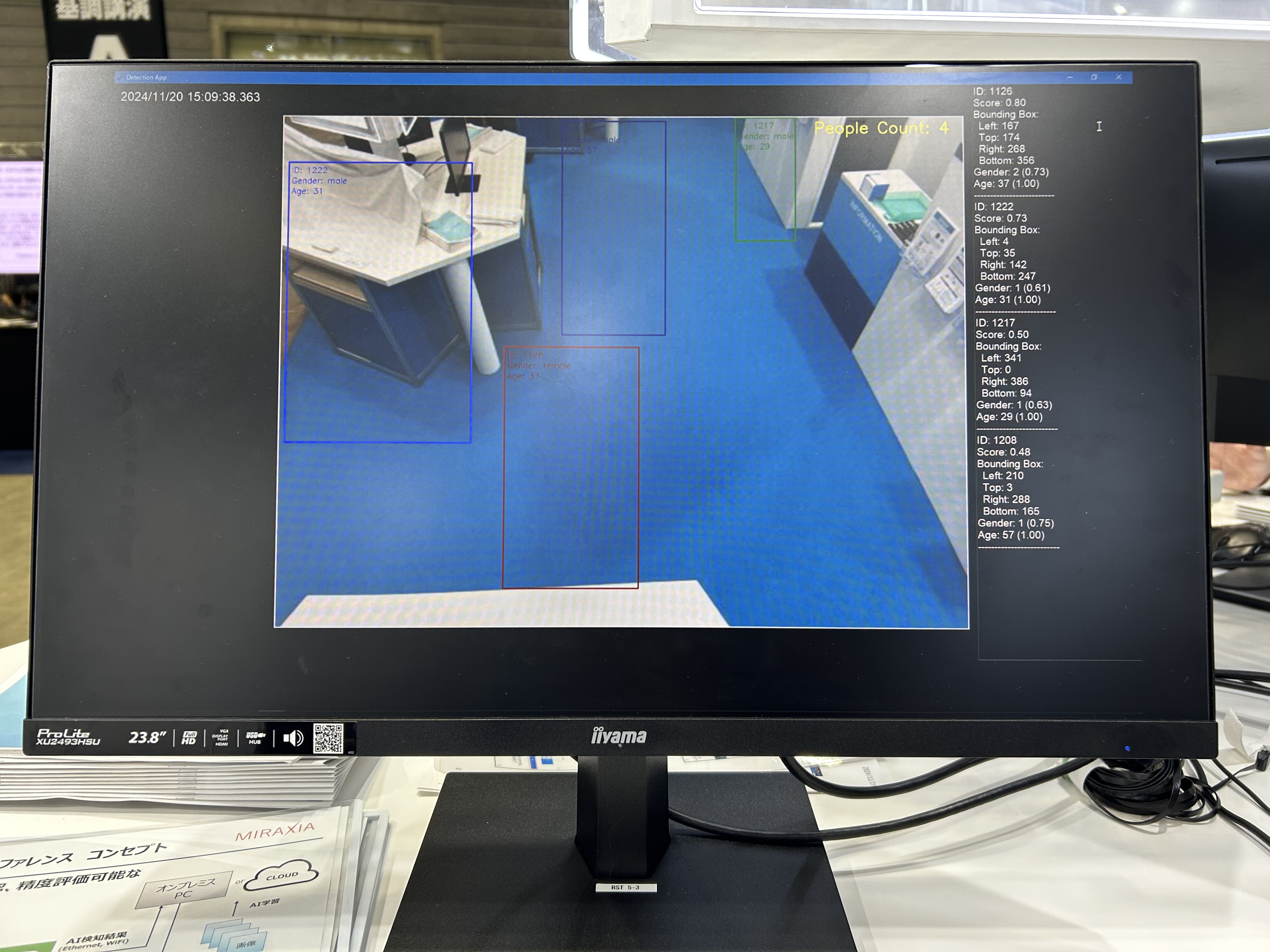 AITRIOSのデモ画面を表示する黒いモニター。画面には青い床面を撮影した映像が表示され、右側には解析データのテキスト情報が並んでいる。エッジAIによる映像解析の様子を示すデモンストレーション画面