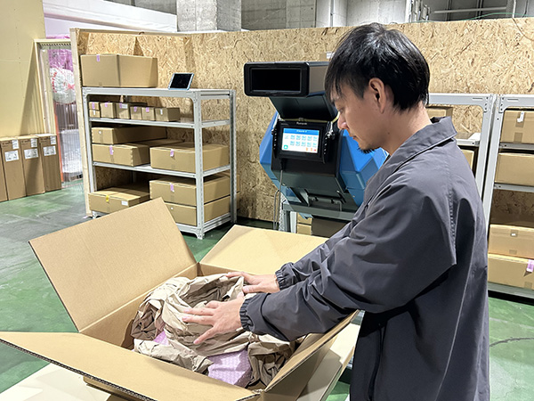 倉庫内で作業員がダンボール箱に紙製緩衝材を設置している様子。背景には保管用の棚とPadPak®Guardian製品が設置されている